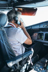 Seitenansicht eines männlichen Flugkapitäns, der über UKW-Funk kommuniziert, während er im Cockpit eines modernen Flugzeugs sitzt und sich auf den Flug vorbereitet - ADSF09175