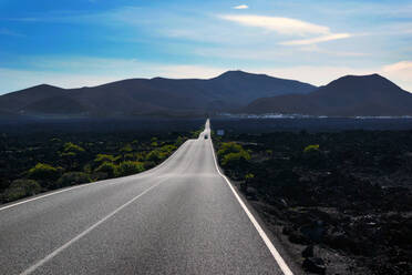 Leere kurvenreiche Straße, die zu einem Bergtal führt, entlang eines dunklen Feldes mit viel Grün auf Lanzarote, Kanarische Inseln, Spanien - ADSF09191