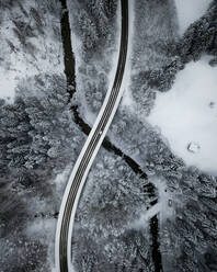 Aerial view of asphalt road stretching over river Ach flowing through snow-covered forest - MALF00053