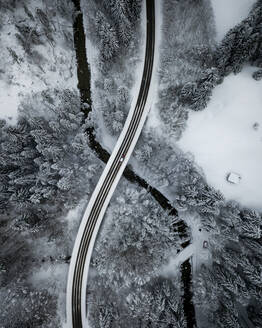 Luftaufnahme einer asphaltierten Straße über den Fluss Ach, der durch einen schneebedeckten Wald fließt - MALF00053