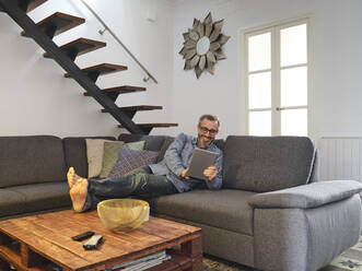 Man talking smiling for a video conference with the tablet alone on the sofa in the living room at home - ADSF09230