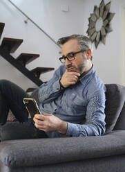 Serious Man using tablet surfing the internet alone on the couch in the living room at home - ADSF09234