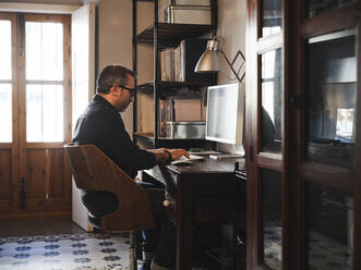 Mann arbeitet zu Hause am Schreibtisch mit Computer über Internet - ADSF09240