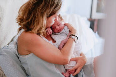 Closeup of loving mother holding adorable newborn baby while sitting on bed at home - ADSF09258