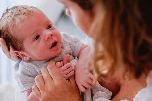 Von oben Nahaufnahme von liebevollen Mutter hält adorable neugeborenes Baby, während auf dem Bett zu Hause sitzen - ADSF09260