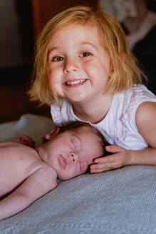 Freudige kleine Ernte Vorschule weiblich berühren mit Interesse ruhigen Säugling mit geschlossenen Augen ruht im Bett gegen unscharfen Innenraum von Licht Schlafzimmer - ADSF09265