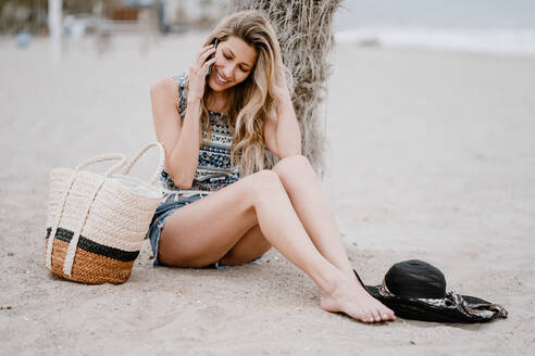 Junge attraktive Frau mit langen Haaren, die sich am Strand entspannt und mit einem Mobiltelefon an einem Sommertag spricht - ADSF09273
