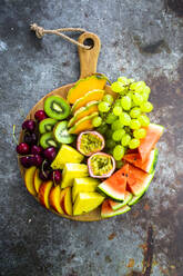 Fruit salad with watermelon, kiwi, passion fruit, grape, cherry, peach and melon on chopping board - GIOF08676