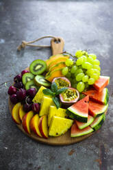 Fruit salad with watermelon, kiwi, passion fruit, grape, cherry, peach and melon on chopping board - GIOF08677