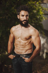 Attractive shirtless man standing in front of shrubs - MIMFF00145