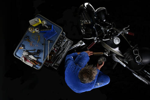 Draufsicht auf einen Mann, der ein altes Motorrad repariert, mit schwarzem Hintergrund (Ardie RZ) - SRSF00657