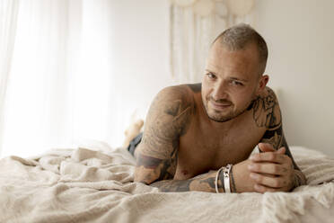 Smiling handsome man relaxing on bed at home - GMLF00409