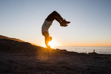 Männlicher Sportler, der bei Sonnenaufgang auf seinen Händen balanciert - CAVF87969