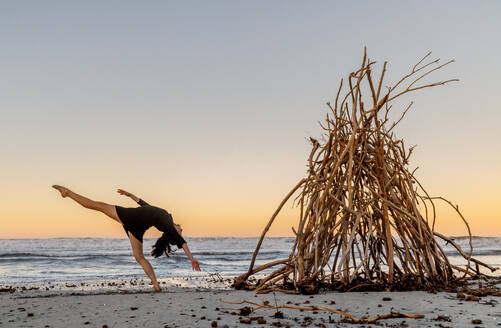 Junge Tänzerin auf Sand Küste mit hölzernen Zweigen für Lagerfeuer in der Nähe wogenden Meer und blauen Himmel platziert - ADSF09343