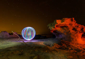 Abstract sphere levitating above rocks and black sky with stars at night - ADSF09348