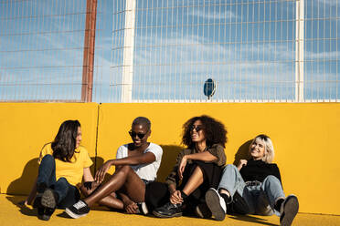 Carefree youthful diverse women in casual clothes laughing and having friendly conversation while sitting in sport playground - ADSF09366