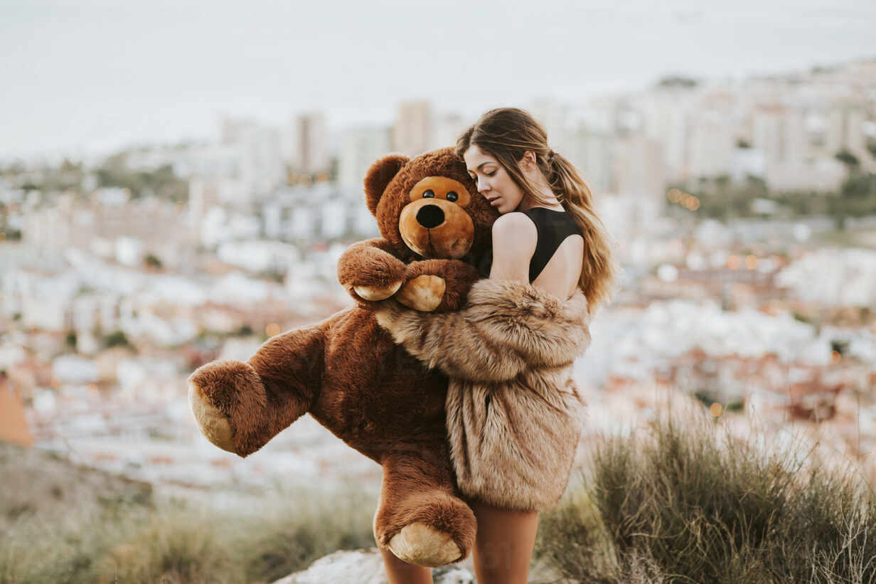Woman with eyes closed hugging teddy bear while standing against