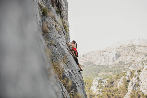 Female rock climber climbing mountain against clear sky stock photo