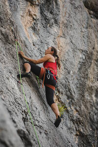 Selbstbewusste Frau klettert mit Seil auf einen felsigen Berg - DMGF00119
