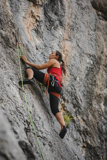 Confident woman climbing rocky mountain using rope - DMGF00119
