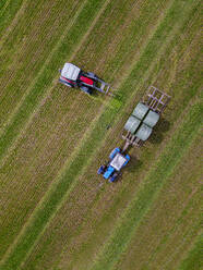 Aerial view of two tractors collecting hay bales in field - KNTF05149