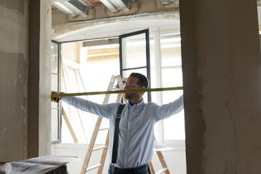 Architect using tape measure in a house under construction - VABF03291