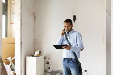 Architekt mit Tablet am Telefon in einem im Bau befindlichen Haus - VABF03296