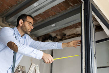 Architekt mit Maßband am Fensterrahmen in einem im Bau befindlichen Haus - VABF03301