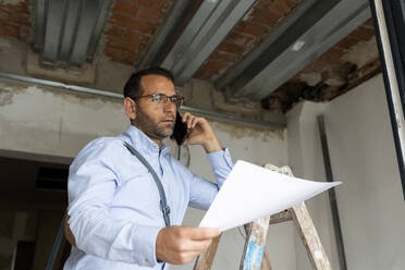 Architekt mit Plan am Telefon in einem im Bau befindlichen Haus - VABF03303