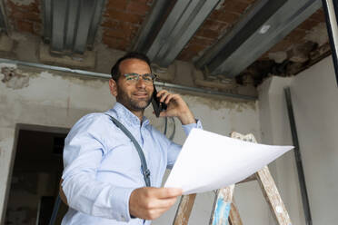Porträt eines selbstbewussten Architekten mit Plan am Telefon in einem im Bau befindlichen Haus - VABF03304