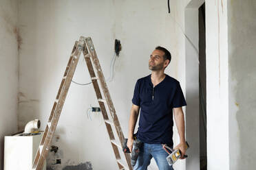 Selbstbewusster Bauarbeiter, der in einem im Bau befindlichen Haus steht - VABF03322