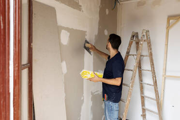 Construction worker plastering wall in a house - VABF03338