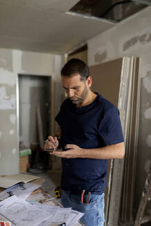 Man using phone in a house under construction - VABF03351