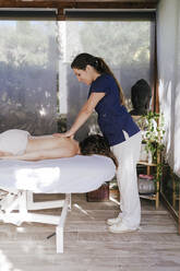 Therapeutin gibt einer Frau, die sich auf einer Liege entspannt, eine Rückenmassage im Wellnessbereich - EBBF00518