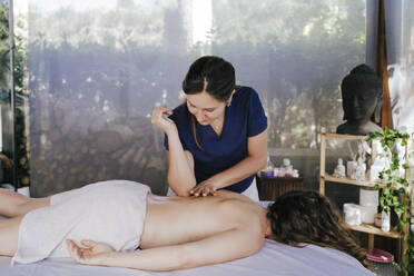 Female therapist massaging shirtless woman's back relaxing on table in spa - EBBF00520