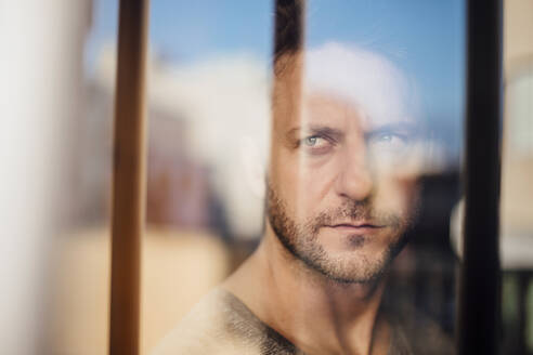 Close-up of thoughtful man looking through window seen through glass - MIMFF00162