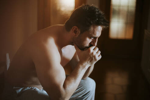 Close-up of shirtless thoughtful man sitting at home - MIMFF00165