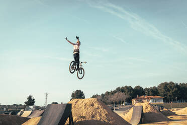 Young man jumping with bicycle against sky at park during sunset - ACPF00781