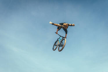 Young man performing stunt with bicycle against blue sky at park during sunset - ACPF00782