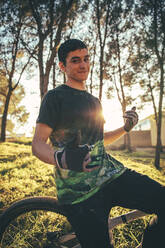 Smiling young man with bicycle standing in park during sunset - ACPF00783