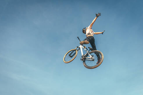 Unbekümmerter Mann, der einen Stunt mit dem Fahrrad gegen den blauen Himmel bei Sonnenuntergang macht - ACPF00784