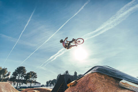 Carefree young man performing stunt with bicycle against blue sky at park during sunset stock photo