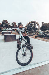 Carefree young man riding bicycle on ramp in park during sunset - ACPF00790