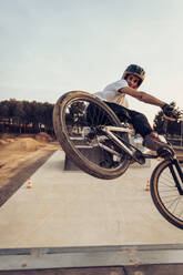 Man wearing helmet riding bicycle on ramp against sky during sunset - ACPF00797