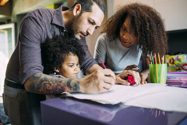 Woman looking at father with daughter drawing on paper at home - MEUF01882