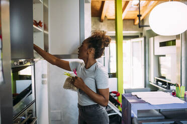 Mid adult woman searching in cabinet at home - MEUF01888