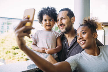 Lächelnde Frau macht Selfie mit Vater und Tochter auf dem Balkon - MEUF01896