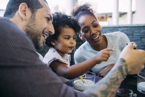 Nahaufnahme einer lächelnden Familie, die auf ihr Smartphone schaut, während sie im Esszimmer sitzt - MEUF01899