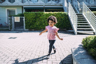 Baby girl with curly hair walking on footpath during sunny day - MEUF01906