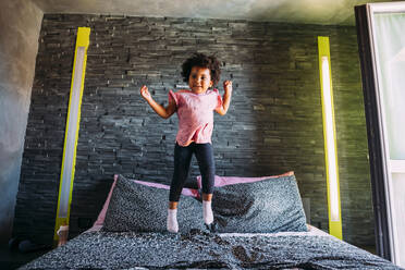 Playful baby girl jumping on bed at home - MEUF01919